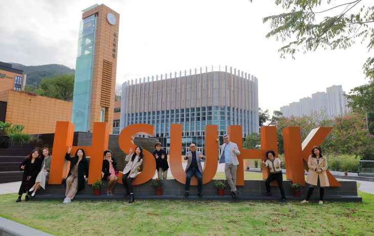 A group photo at the Wei Lun Square, an open plaza with a green courtyard, with the abbreviation of the University.